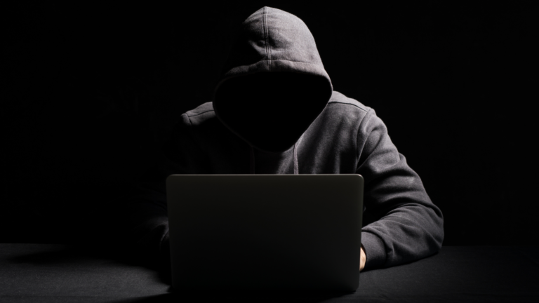 Computer Hacker in dark clothing using a laptop